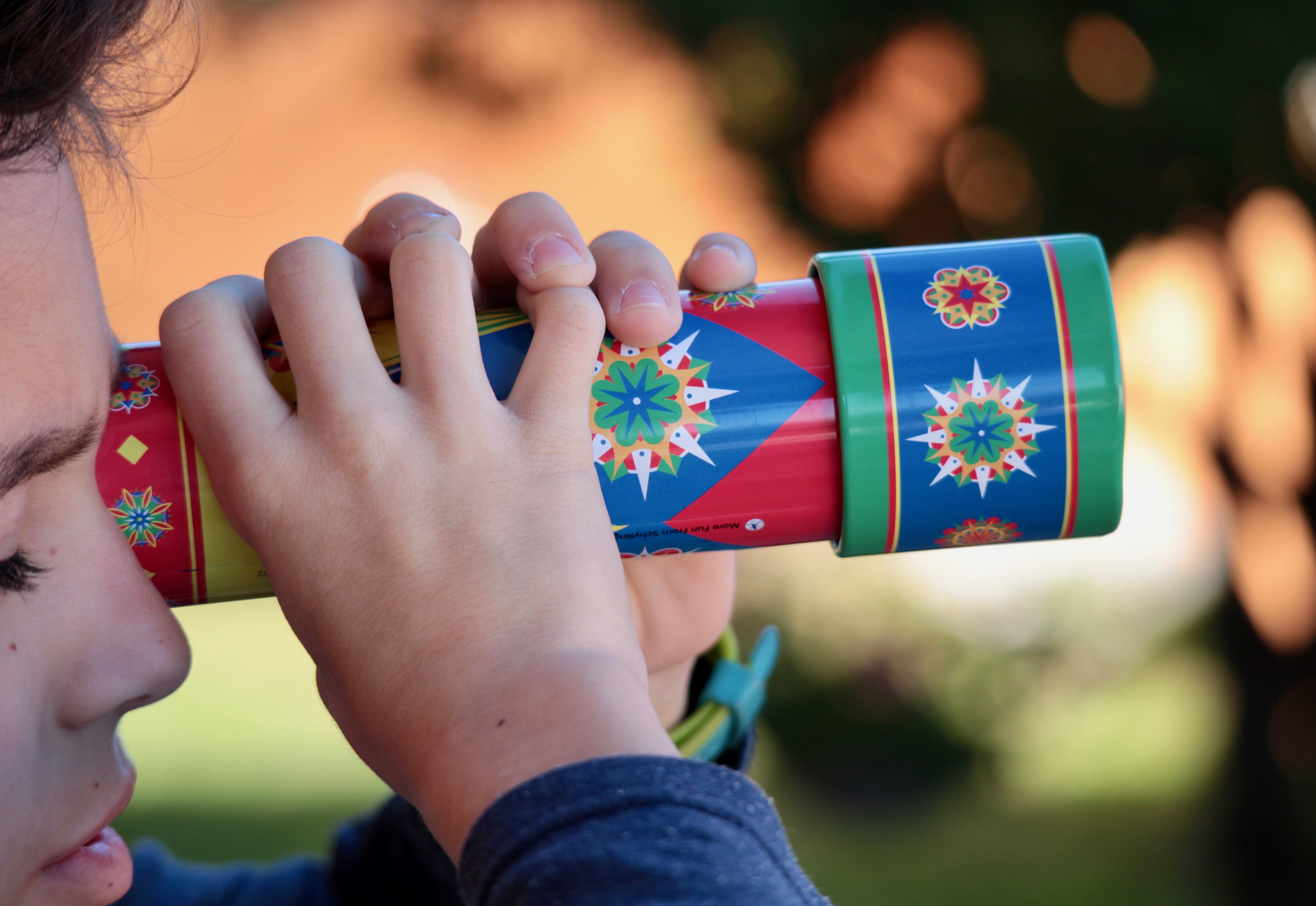 Young boy holding a kaleidoscope up to her eyes.