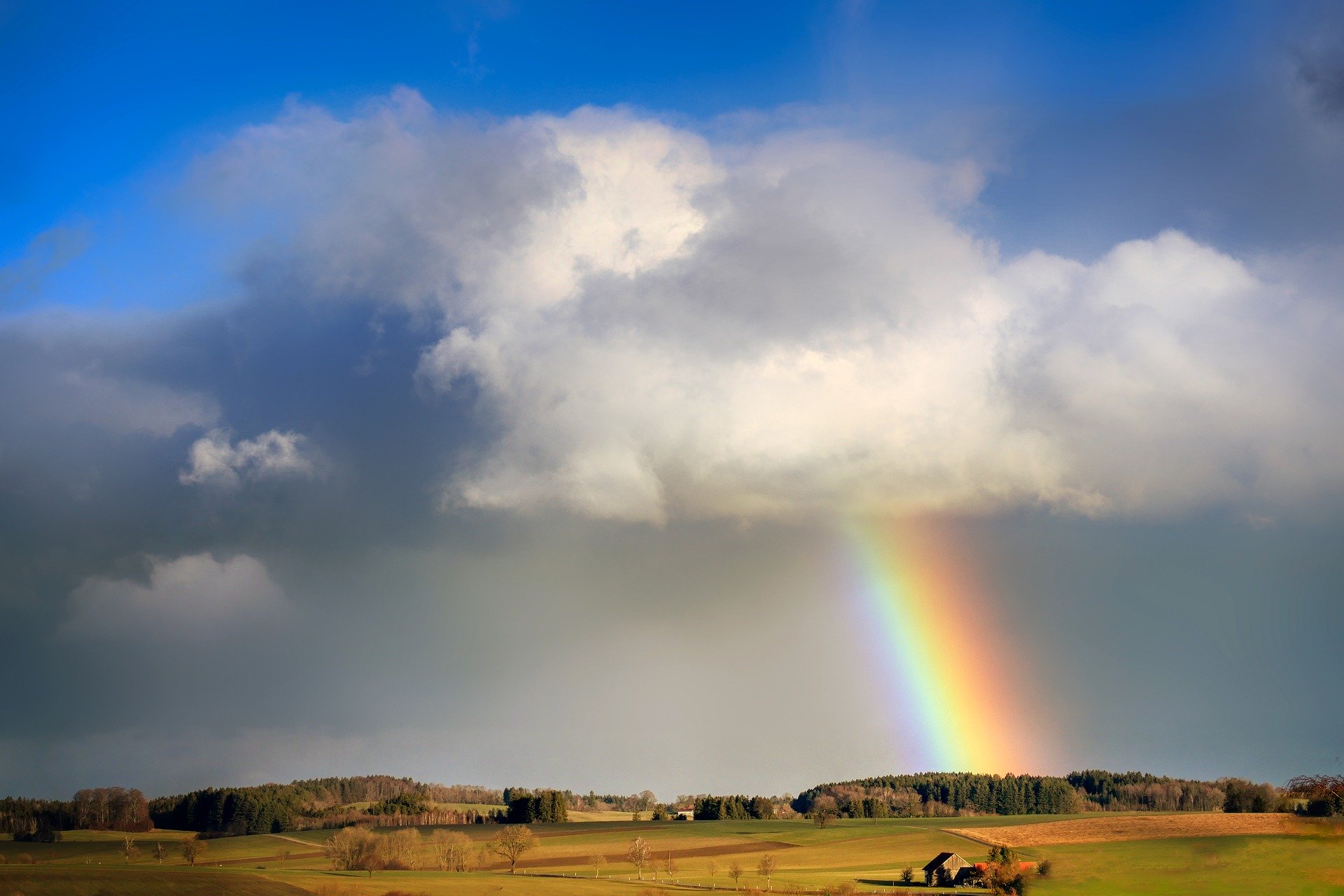Rainbow appearing out of a cloud over a countryside.