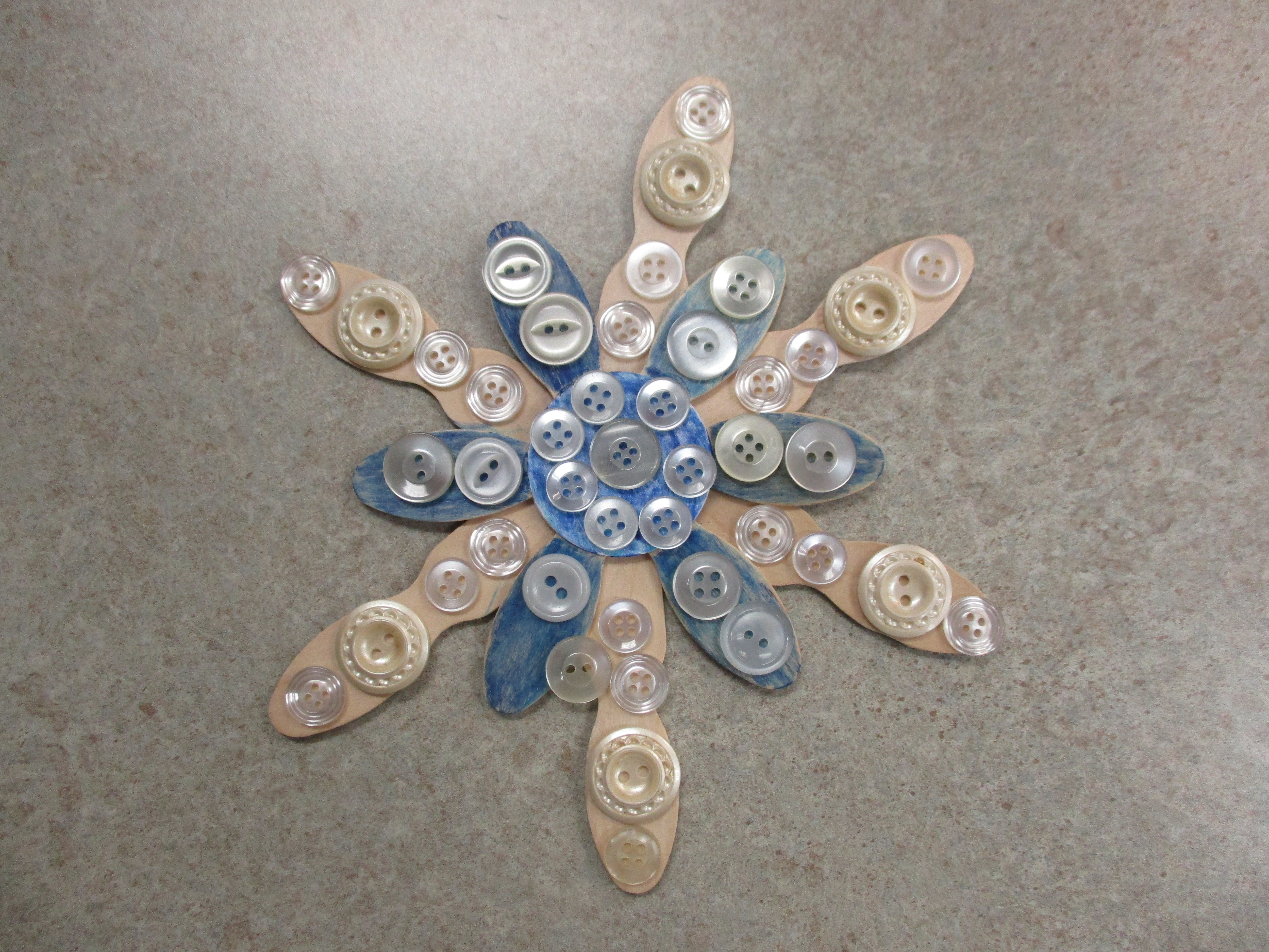 Snowflake ornament made out of buttons and popsicle sticks.