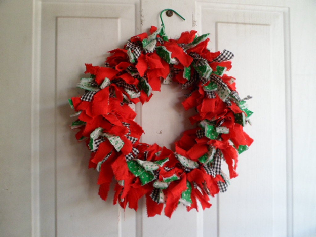 A red and green fabric wreath hanging on a door.