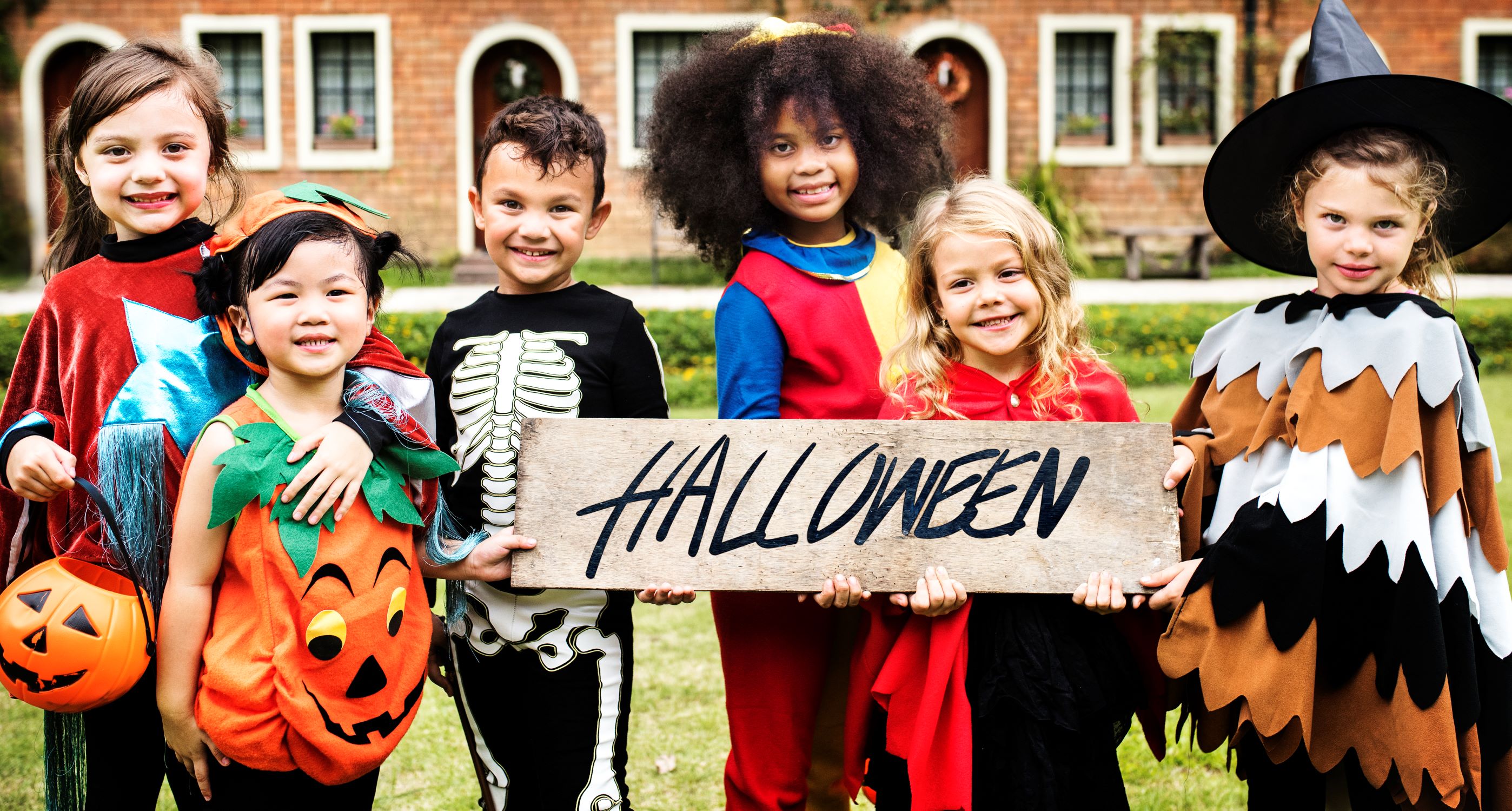 Children dressed in Halloween costumes holding a sign saying Halloween.