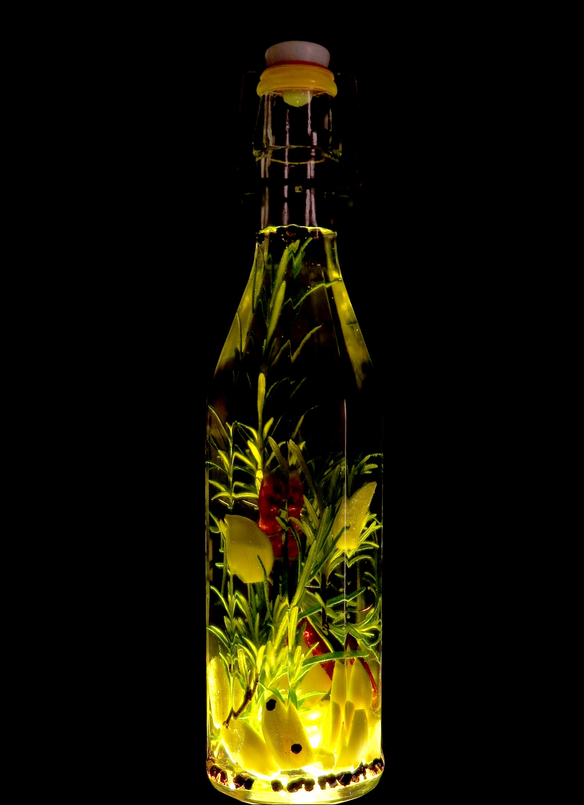 Bottle of oil with herbs inside on a black background.