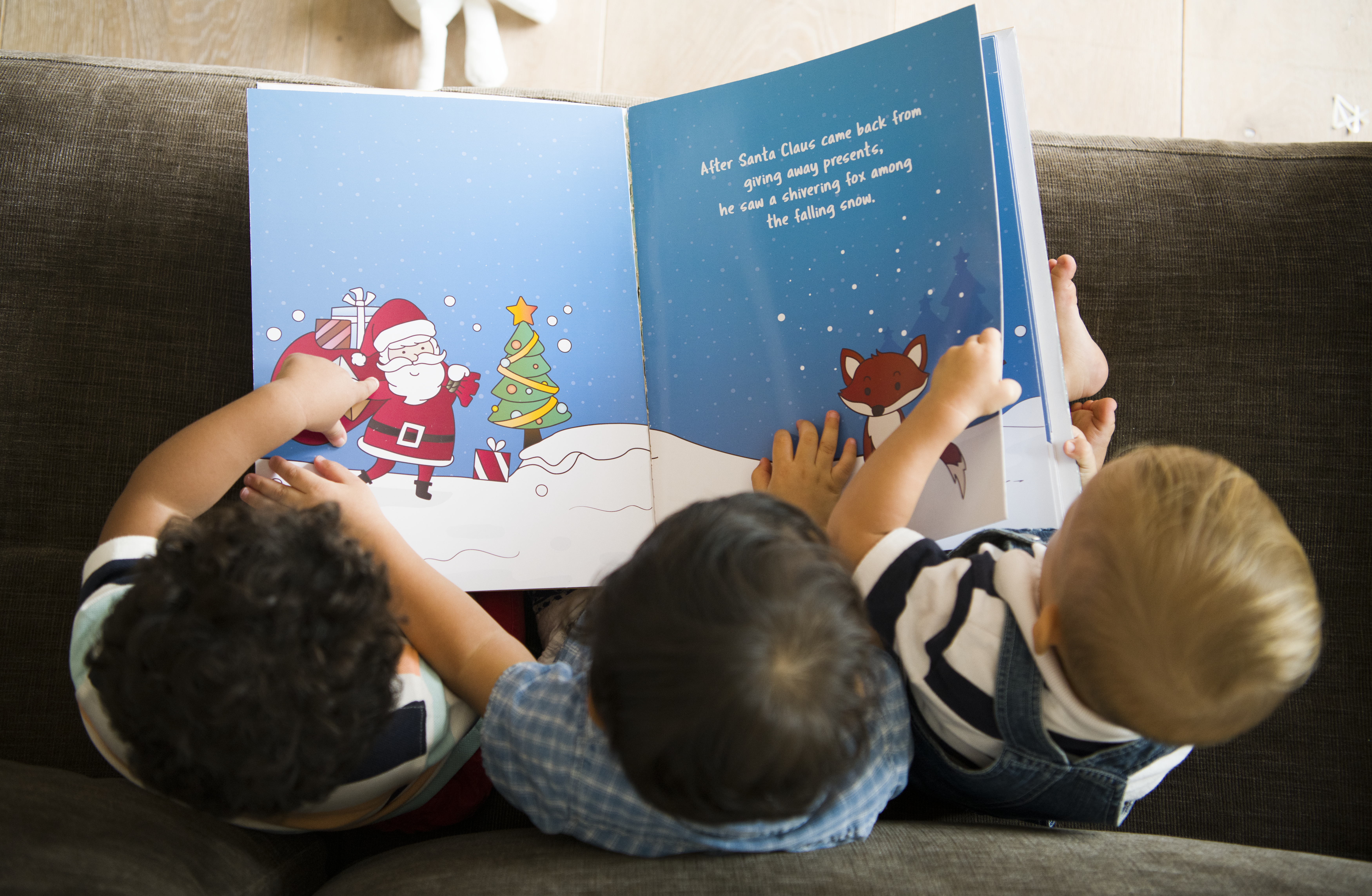 Three babies on a couch holding a Christmas book.