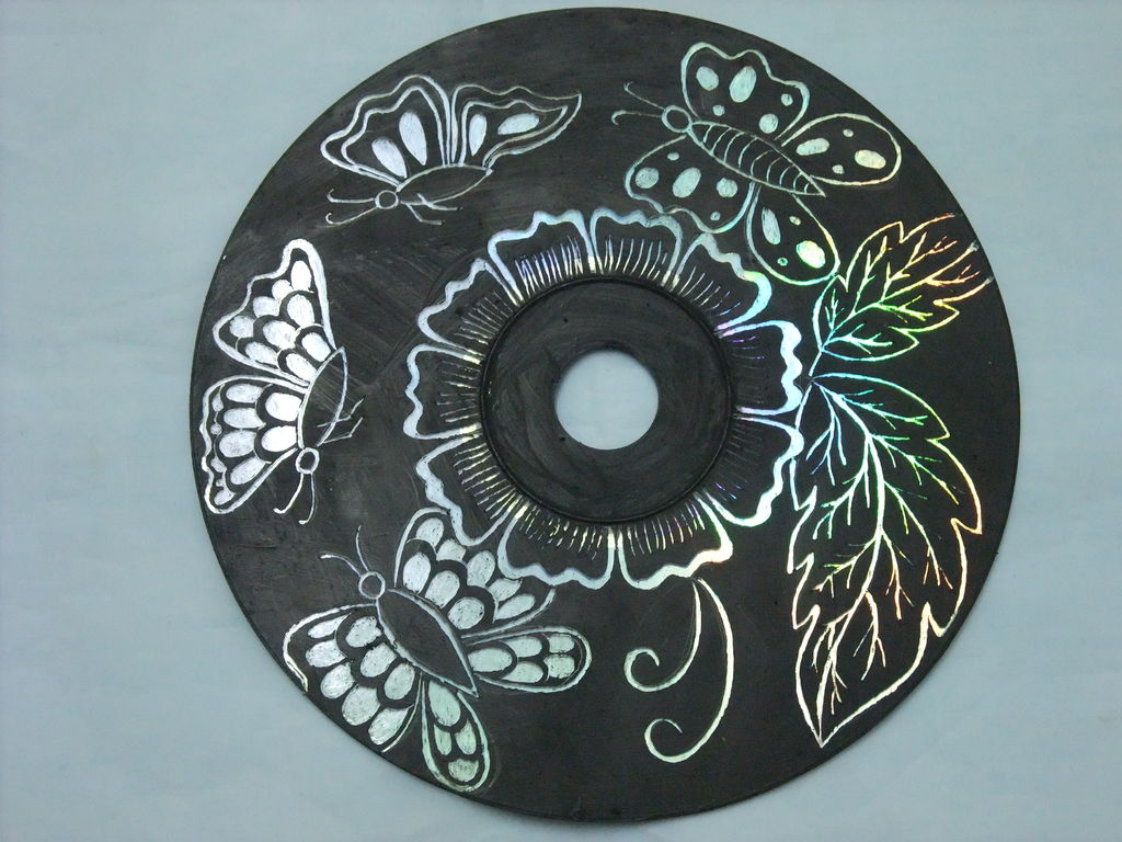 A painted CD with butterflies, a flower. and leaves scratched through the paint surface.