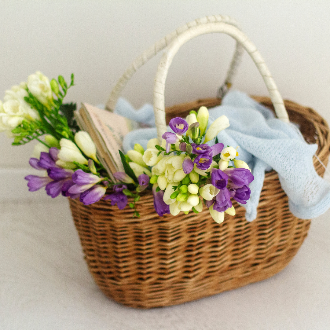 Basket holding flowers, a book, and a blue blanket.