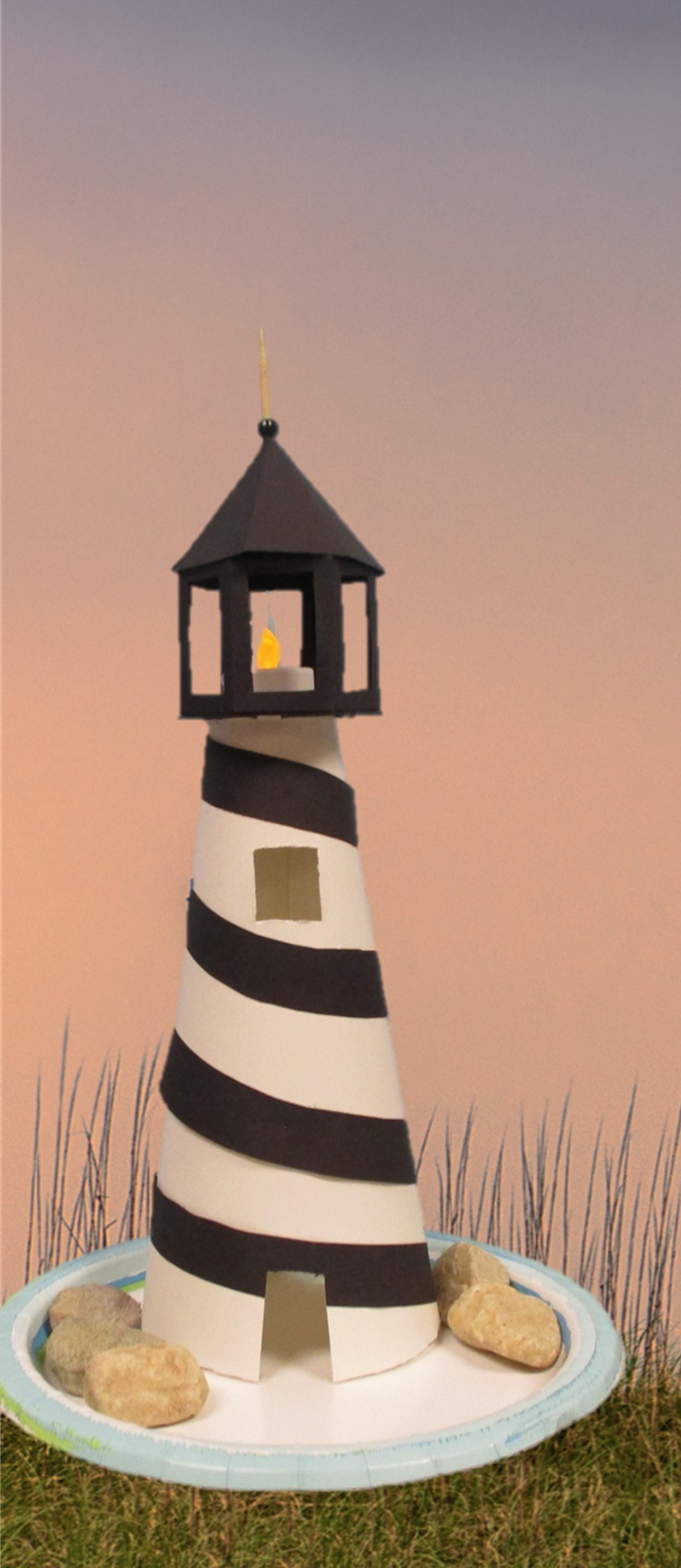 Paper lighthouse on a plate with rocks on a photo background.