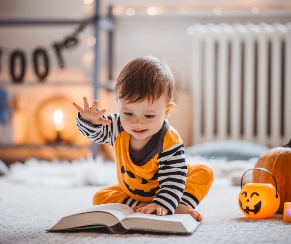 Baby in a Jack-O-Lantern Onesie with a book.