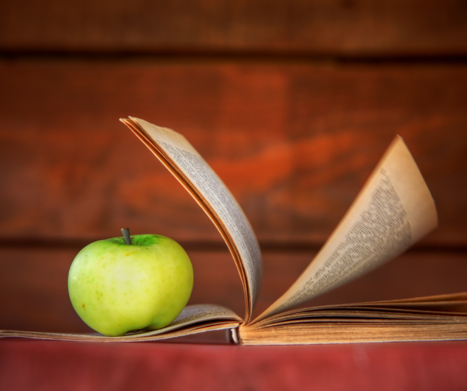 Green Apple sitting on an open book.
