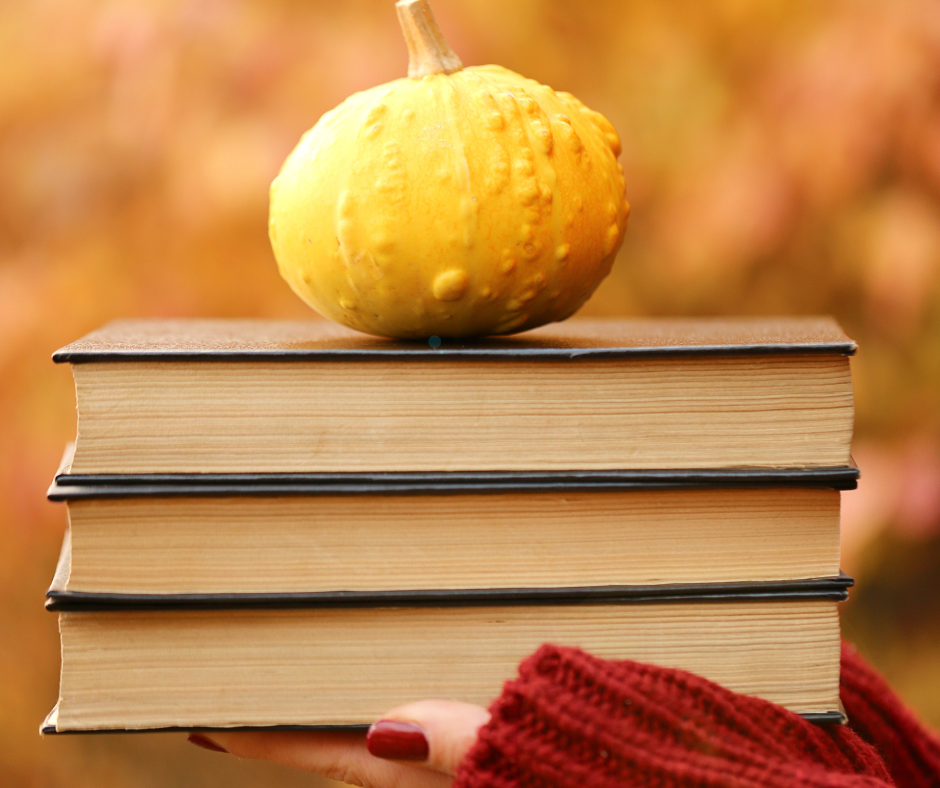 Woman in a red sweaters hand holding 3 books and a small pumpkin.