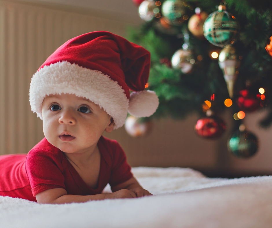 Baby in a Santa hat next to a treee