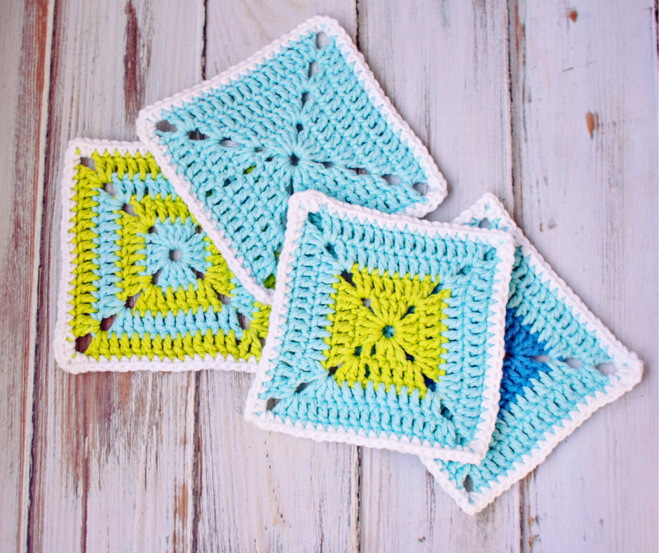 Four overlapping crochet squares in shades of lime green, white, and blue on a white washed wood background.