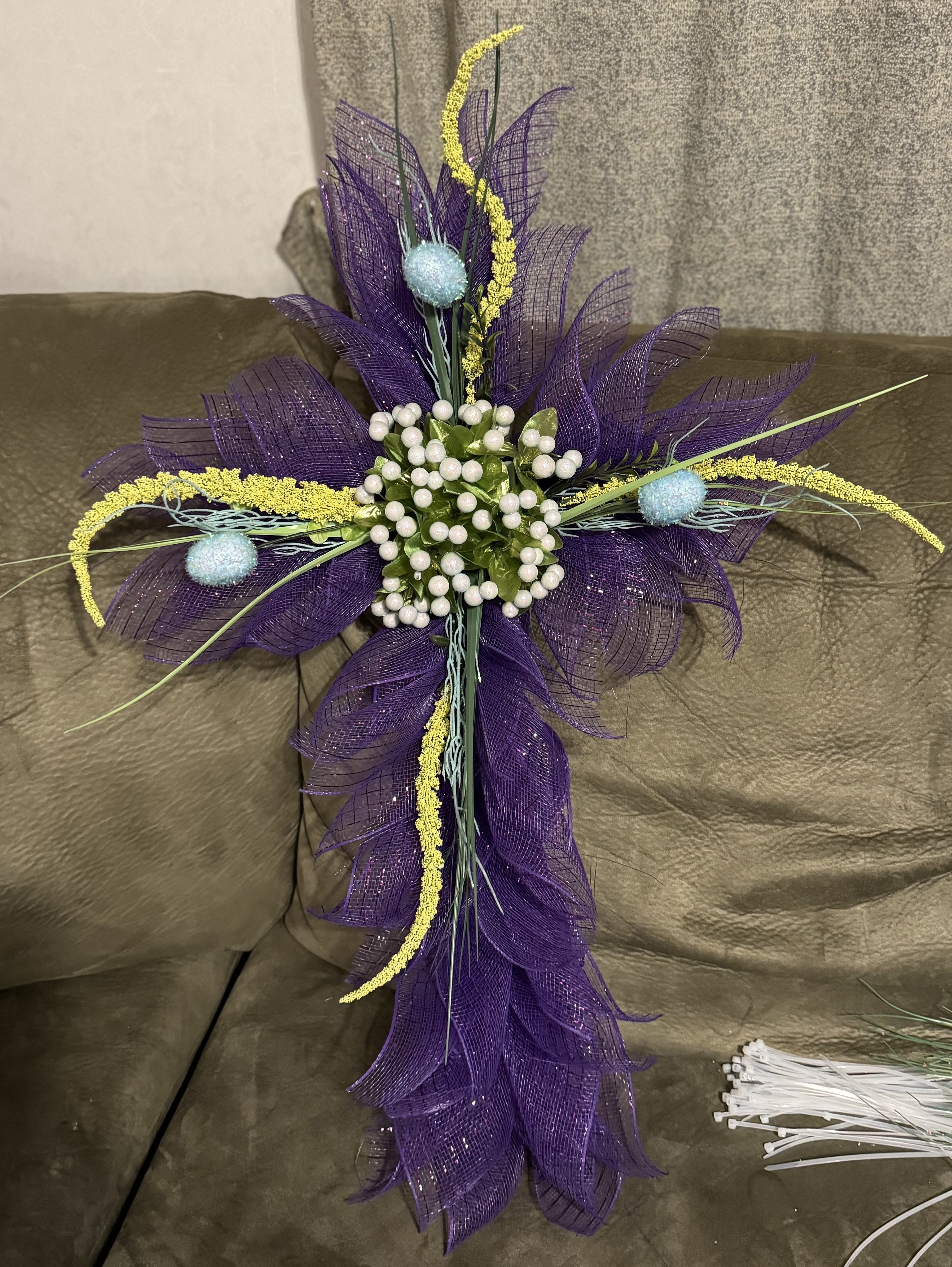 Wreath made of purple ribbon in the shape of a cross with yellow, blue, and white accents. 