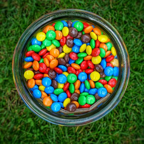 M&Ms in a clear jar in the grass.