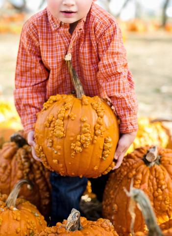 Young boy holding a large pumpkin.