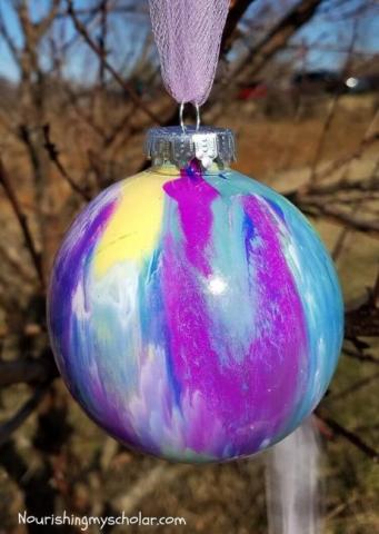 Shades of blue, purple, white and yellow paint swirled inside a clear Christmas ornament.