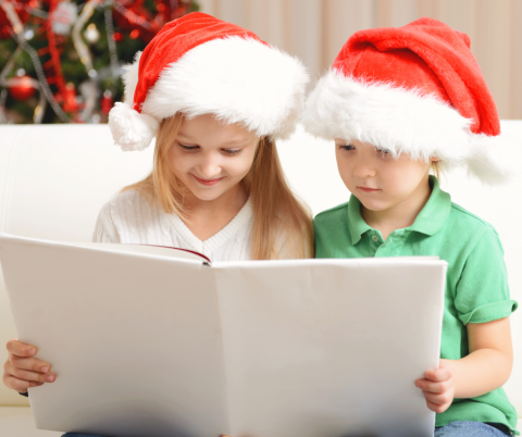 Two children reading a book while wearing Santa Hats.