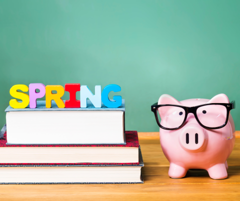 Books, a piggy bank with glasses, and letters spelling out SPRING in front of a green chalkboard.