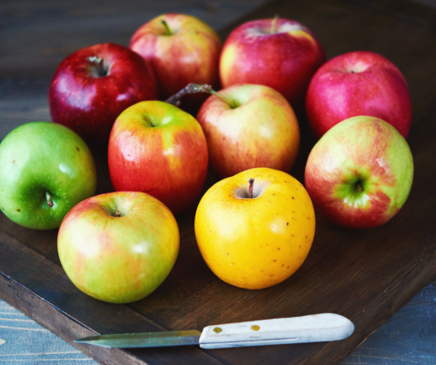 Different types of apples on a cutting board with a knife.