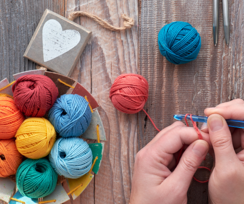 Colorful bowl of yarn and hands holding a crochet hook.