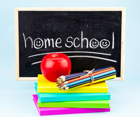 Small blackboard with the word homeschool on it and a stack of neon books, colored pencils, and a red apple.