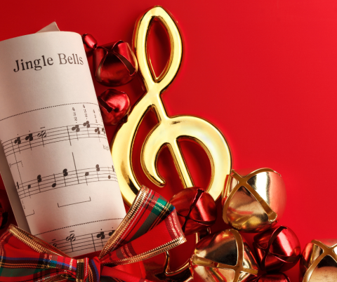 Rolled up scroll of Christmas music, bells, and a gold music note on a red background.