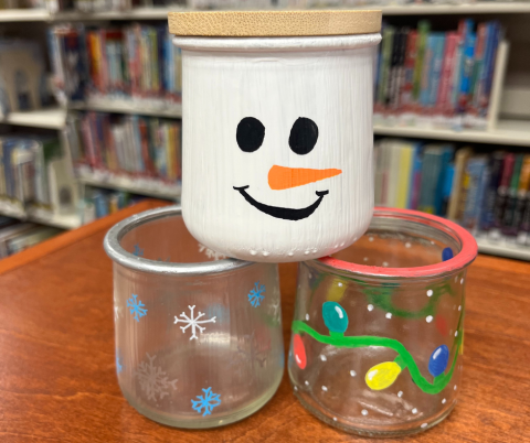 3 winter/holiday painted jars stacked on top of each other on a table in a library.
