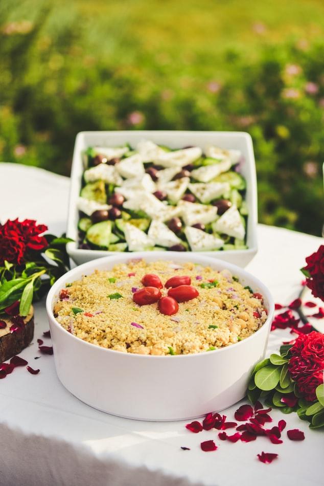 Photo of Mediterranean style food on a table with red flowers.