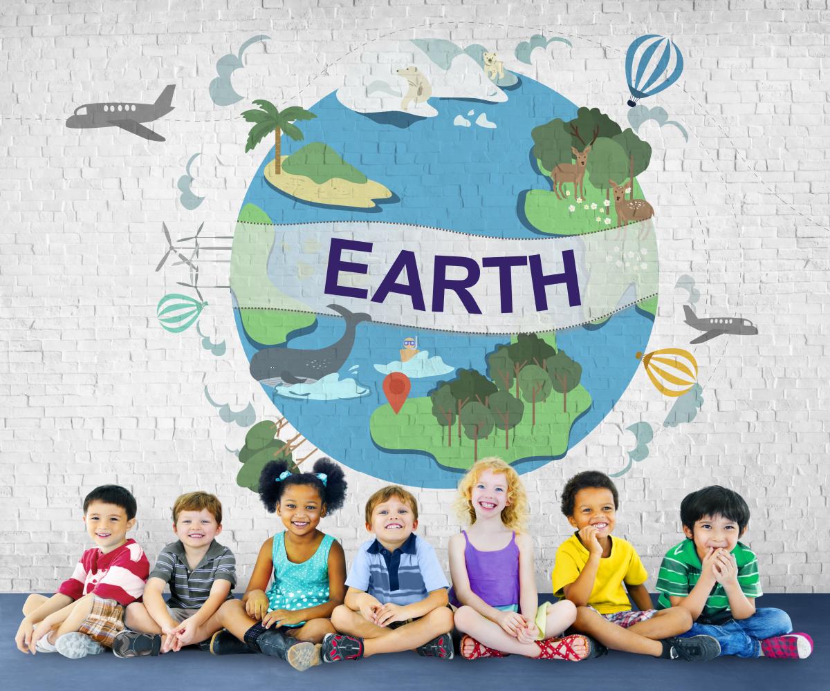 Group of kids sitting in front of a white brick wall with a stylized image of the Earth with trees, animals, planes, hot air balloons and more.