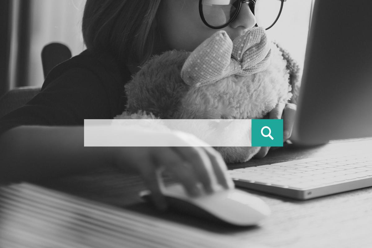 Black and white image of a young girl looking at a computer screen with a search bar.