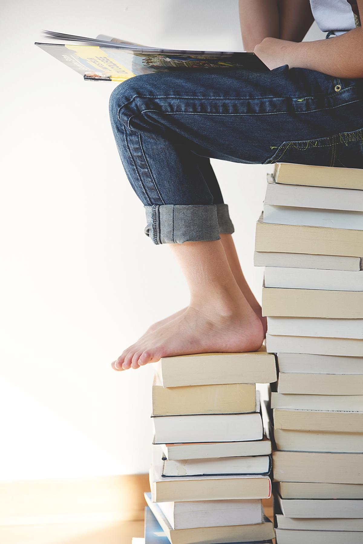 Child sitting on a stack of a books reading.