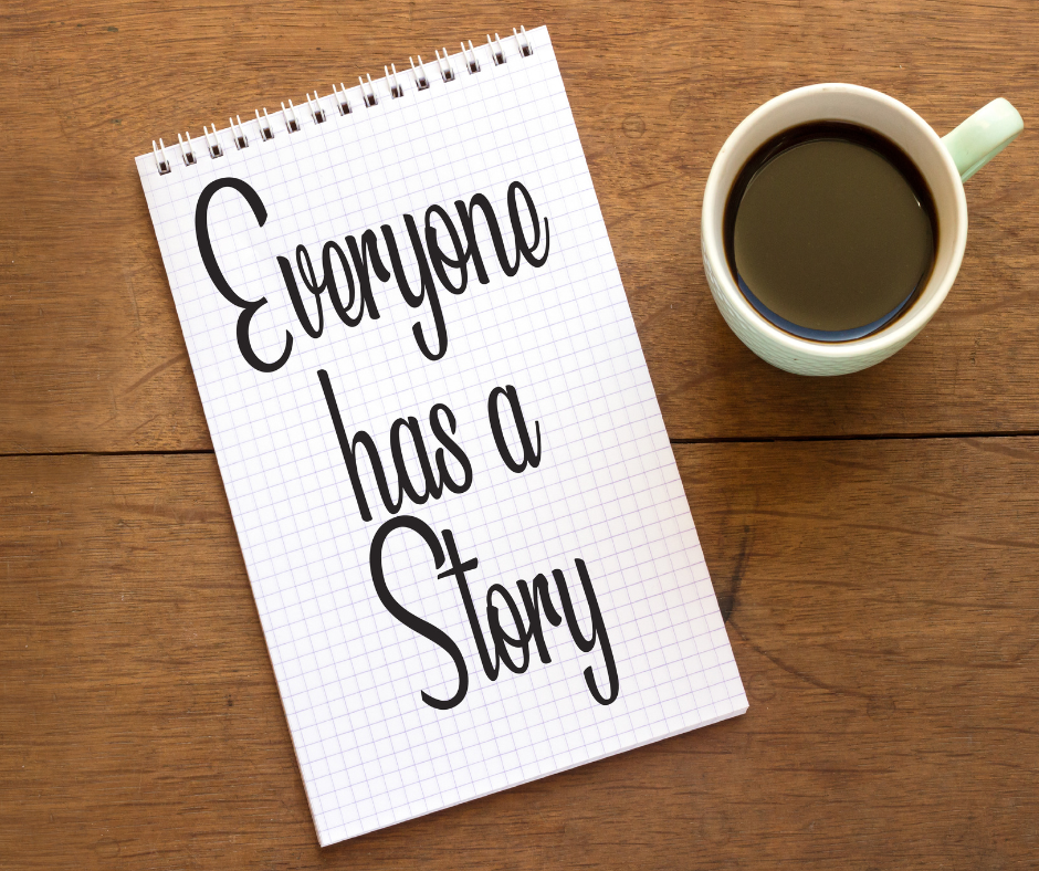 Notebook that has the phrase "Everyone has a story" written on it and a cup of copy on a wooden surface