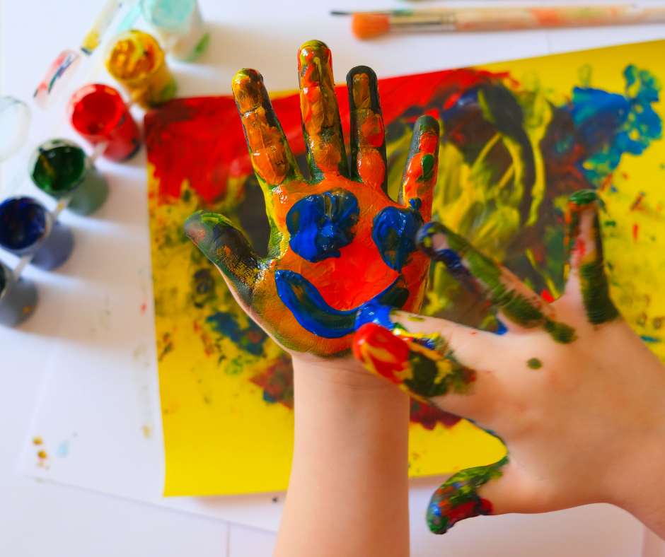Child's hand covered in paint and a messy canvas.